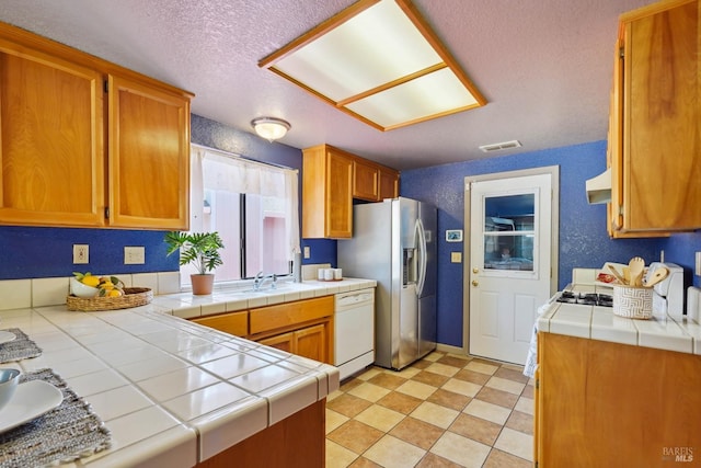 766 Morissette Way, Vacaville, CA 95687 - kitchen featuring white dishwasher, tile counters, stainless steel fridge, a sink, and a textured ceiling