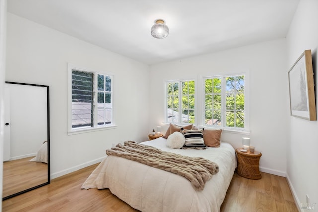 bedroom with multiple windows, light wood-type flooring, and baseboards
