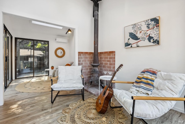 sitting room featuring a wall mounted AC, a wood stove, wood finished floors, and a skylight