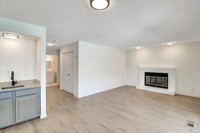181 Belvedere Ct, Vallejo, CA 94589 - unfurnished living room with a sink, light wood-style flooring, a brick fireplace, a textured ceiling, and baseboards