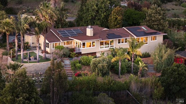 rear view of house featuring roof mounted solar panels, stairway, a chimney, and fence