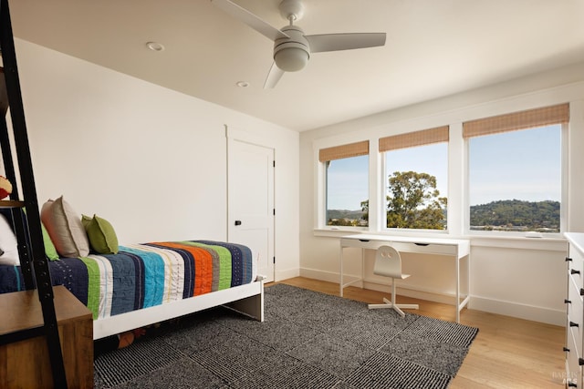 bedroom with multiple windows, light wood finished floors, and baseboards