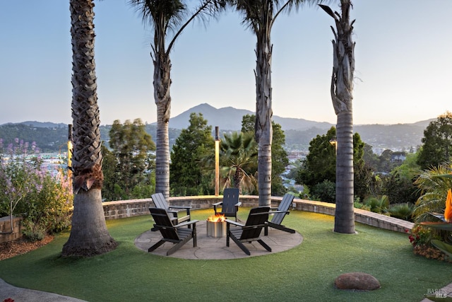 yard at dusk with a fire pit, a mountain view, a patio, and a lawn