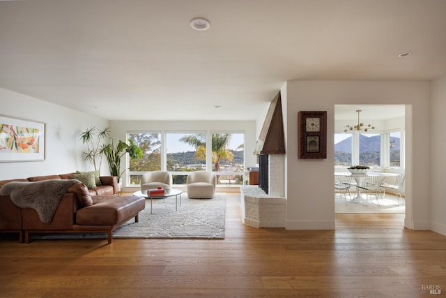 living room featuring a chandelier, healthy amount of natural light, light wood-type flooring, and a brick fireplace