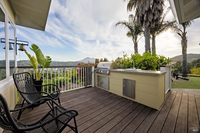 wooden deck with a mountain view, grilling area, an outdoor kitchen, and a sink