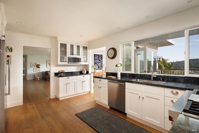kitchen featuring appliances with stainless steel finishes, a sink, white cabinetry, light wood-style flooring, and glass insert cabinets