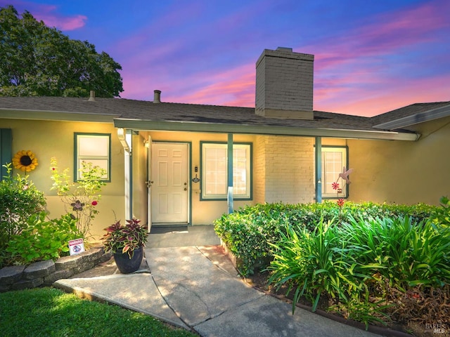 1233 Lincoln St, Fairfield, CA 94533 - exterior entry at dusk featuring a chimney, a shingled roof, and stucco siding