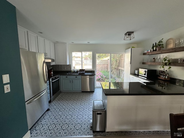 3 Aries Ln, Novato, CA 94947 - kitchen with appliances with stainless steel finishes, a peninsula, under cabinet range hood, dark countertops, and decorative backsplash