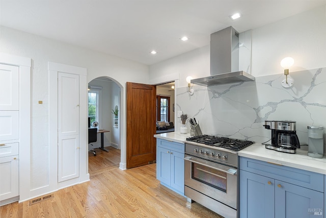 439 4th St E, Sonoma, CA 95476 - kitchen featuring stainless steel stove, wall chimney exhaust hood, arched walkways, light wood finished floors, and decorative backsplash