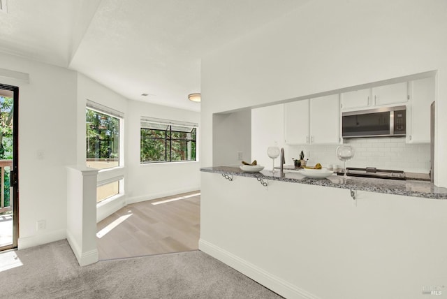 21100 Gary Dr Unit 215, Hayward, CA 94546 - kitchen featuring stainless steel microwave, dark stone counters, decorative backsplash, a breakfast bar, and white cabinets