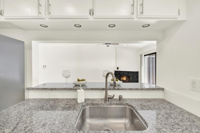 21100 Gary Dr Unit 215, Hayward, CA 94546 - kitchen with a sink, light stone countertops, white cabinets, a stone fireplace, and a ceiling fan