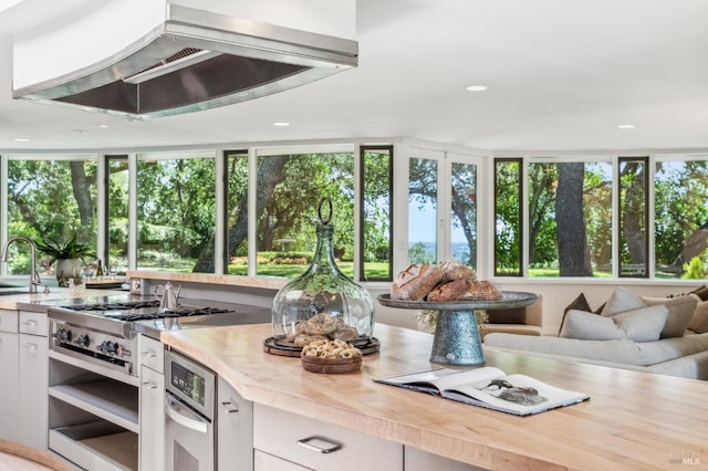 5768 Silverado Trl, Napa, CA 94558 - kitchen with wall chimney exhaust hood, open floor plan, a sink, white cabinetry, and wood counters