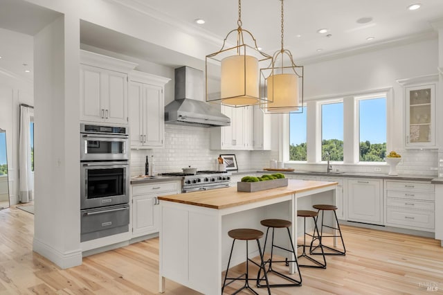30 Sandy Ln, Mill Valley, CA 94941 - kitchen featuring butcher block countertops, a warming drawer, wall chimney exhaust hood, appliances with stainless steel finishes, and a breakfast bar