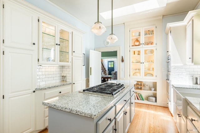 406 Franklin St, Napa, CA 94559 - kitchen featuring stainless steel gas cooktop, decorative backsplash, light wood-style flooring, hanging light fixtures, and glass insert cabinets