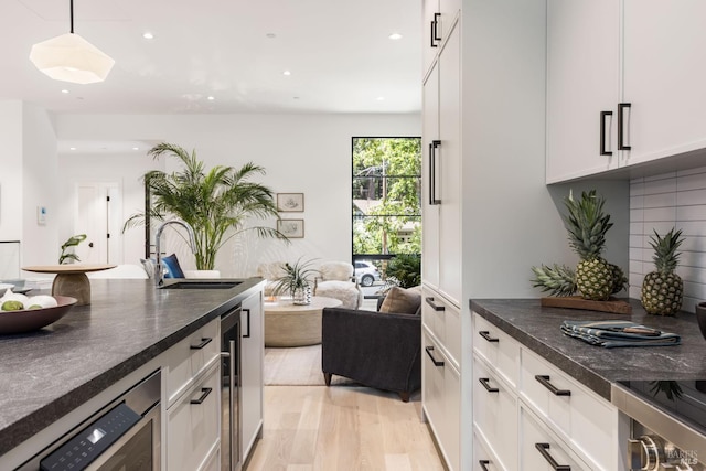 225 W Baltimore Ave, Larkspur, CA 94939 - kitchen with dark countertops, white cabinetry, a sink, hanging light fixtures, and light wood-style flooring