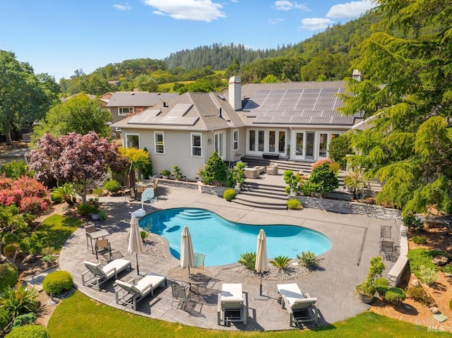 4588 Bennett Valley Rd, Santa Rosa, CA 95404 - back of house with an outdoor pool, a patio, a wooded view, a chimney, and solar panels