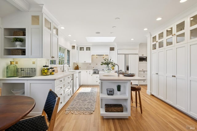 37 Rancheria Rd, Kentfield, CA 94904 - kitchen with open shelves, light wood-type flooring, a sink, built in appliances, and a center island with sink