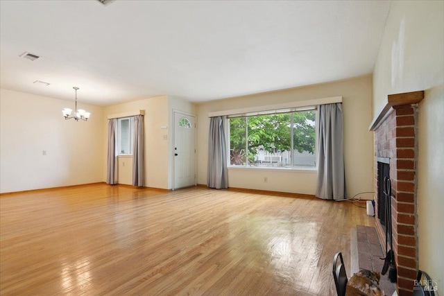 unfurnished living room with a brick fireplace, a chandelier, and light wood finished floors