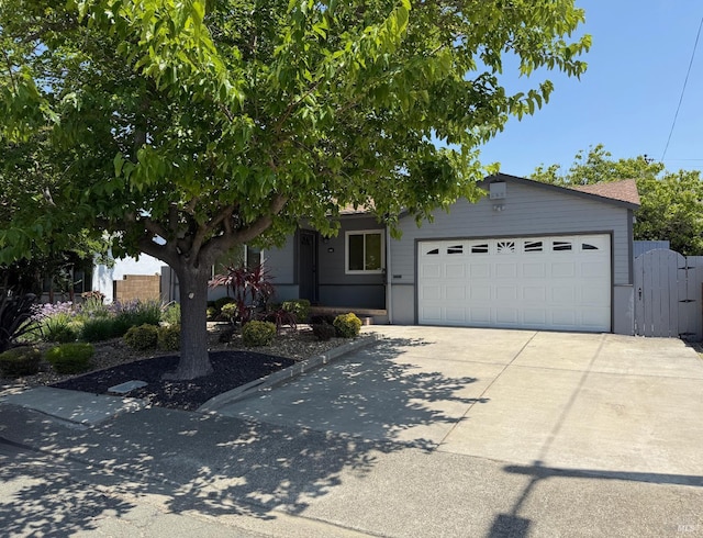 view of property hidden behind natural elements featuring a garage, concrete driveway, and a gate