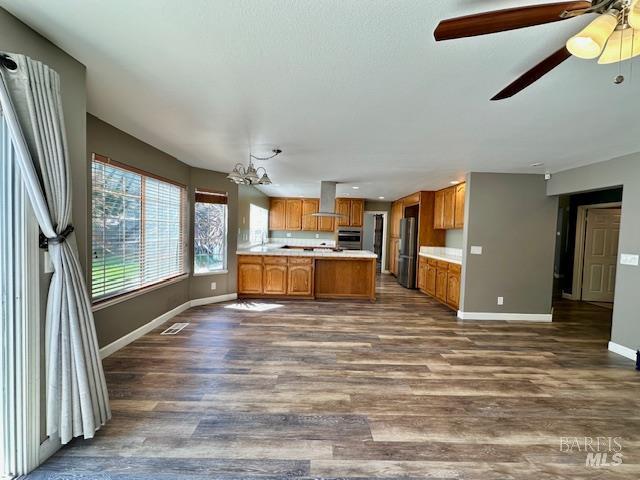 1540 Mccarthy Ct, Dixon, CA 95620 - kitchen with brown cabinets, wall chimney exhaust hood, stainless steel oven, light countertops, and a peninsula