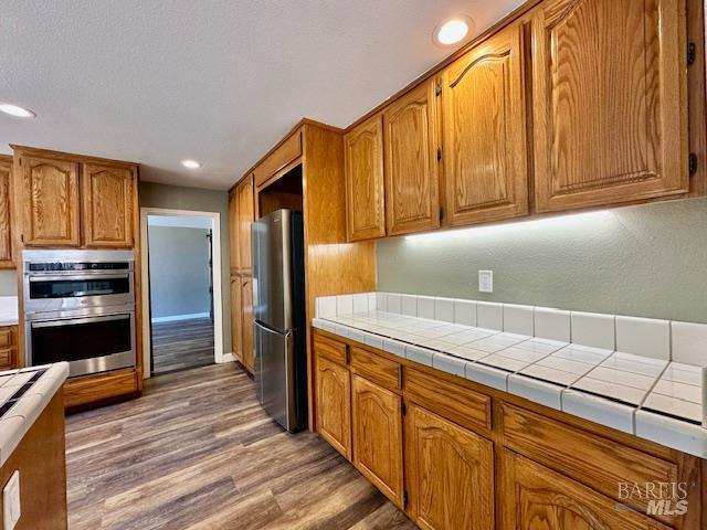1540 Mccarthy Ct, Dixon, CA 95620 - kitchen featuring stainless steel appliances, light wood finished floors, brown cabinetry, recessed lighting, and tile countertops