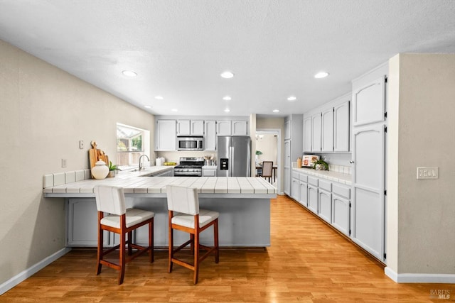 431 Inverness Way, Vacaville, CA 95687 - kitchen featuring tile countertops, appliances with stainless steel finishes, a peninsula, a kitchen bar, and light wood finished floors