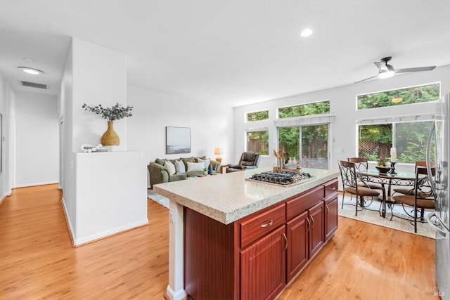 2832 Parkview Ter, Fairfield, CA 94534 - kitchen featuring stainless steel gas cooktop, reddish brown cabinets, light wood-type flooring, a ceiling fan, and a center island