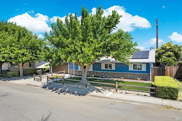 216 Walnut St, Suisun City, CA 94585 - view of front facade with a fenced front yard, stone siding, roof mounted solar panels, an attached garage, and driveway