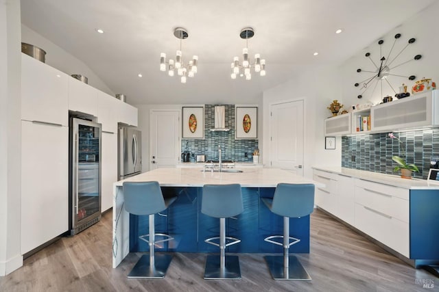 kitchen featuring lofted ceiling, modern cabinets, decorative backsplash, wall chimney exhaust hood, and a chandelier