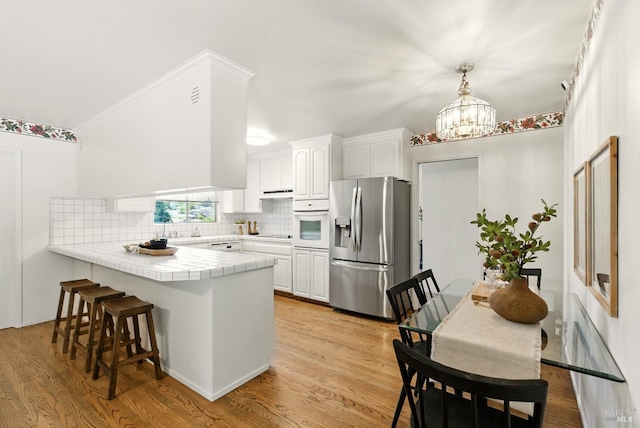 7 Arlene Ct, Petaluma, CA 94952 - kitchen featuring stainless steel refrigerator with ice dispenser, oven, a peninsula, tile countertops, and white cabinetry