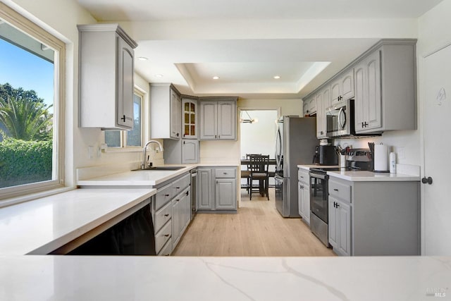 196 Caldwell Dr, Vacaville, CA 95687 - kitchen with gray cabinetry, appliances with stainless steel finishes, light wood finished floors, a tray ceiling, and glass insert cabinets