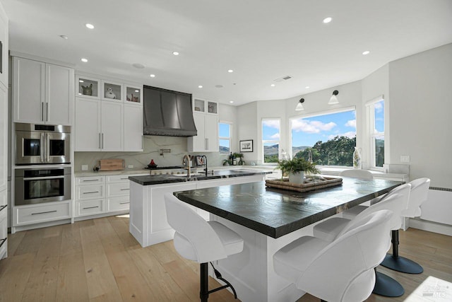 5313 Autumn Rock Ct, Fairfield, CA 94534 - kitchen featuring custom exhaust hood, a center island with sink, light wood-type flooring, recessed lighting, and glass insert cabinets