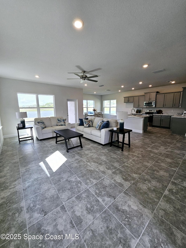 living room with ceiling fan, a water view, sink, and a textured ceiling