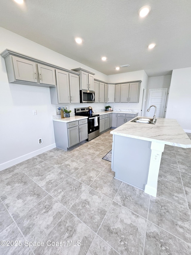 kitchen featuring sink, appliances with stainless steel finishes, a kitchen island with sink, and gray cabinetry