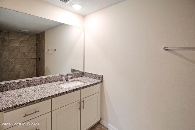 bathroom featuring vanity, a textured ceiling, and tiled shower