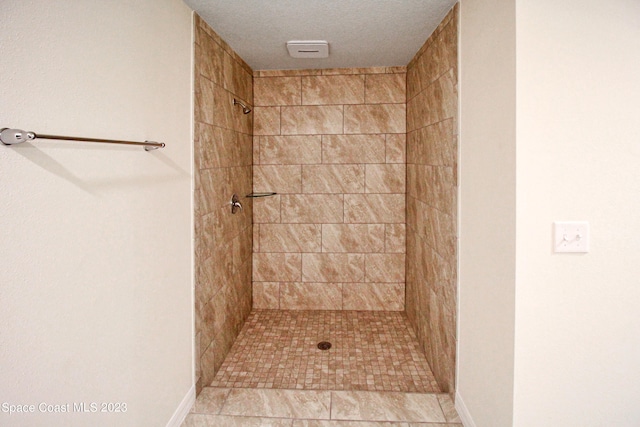 bathroom with a textured ceiling, tile patterned floors, and tiled shower