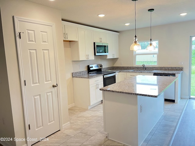 kitchen with a center island, sink, white cabinetry, appliances with stainless steel finishes, and decorative light fixtures