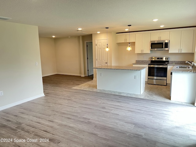 kitchen with pendant lighting, light wood-type flooring, sink, white cabinetry, and appliances with stainless steel finishes