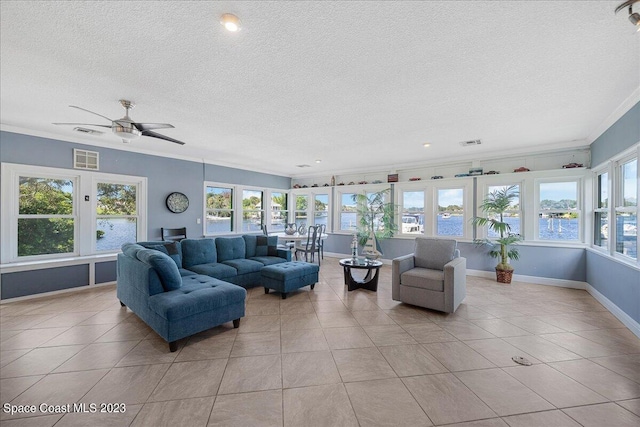 tiled living room featuring a healthy amount of sunlight, ornamental molding, ceiling fan, and a textured ceiling