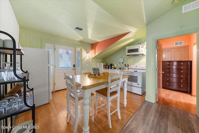 kitchen featuring lofted ceiling, white appliances, a textured ceiling, and light hardwood / wood-style flooring