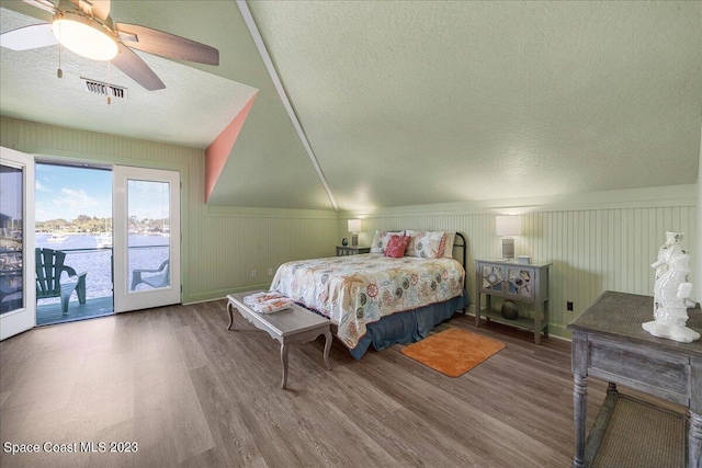 bedroom with a textured ceiling, access to exterior, hardwood / wood-style flooring, and a water view