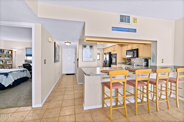 kitchen featuring black appliances, light tile flooring, a breakfast bar, sink, and a textured ceiling