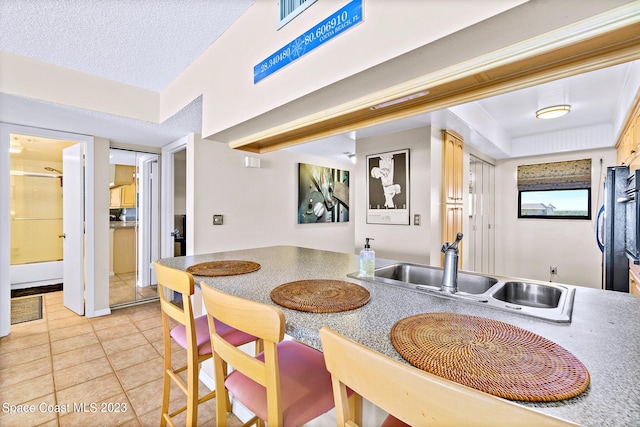 kitchen with light tile floors, light brown cabinets, a textured ceiling, and sink