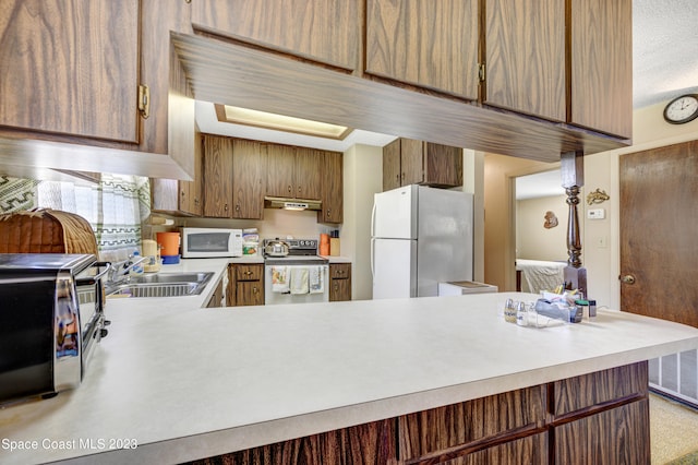 kitchen with white appliances, kitchen peninsula, and sink