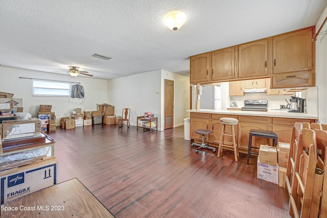 kitchen with ceiling fan, stove, white refrigerator, a breakfast bar area, and dark wood-type flooring