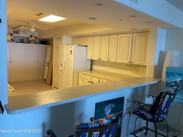 kitchen featuring ceiling fan, white cabinets, light tile flooring, white fridge with ice dispenser, and a kitchen bar