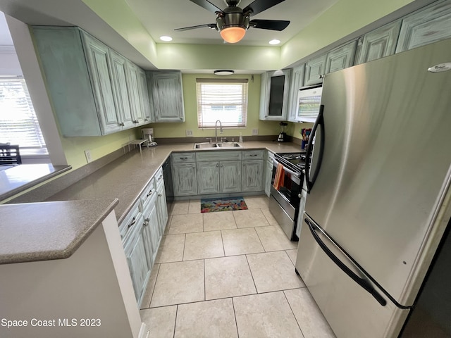 kitchen with ceiling fan, sink, a raised ceiling, stainless steel appliances, and light tile flooring