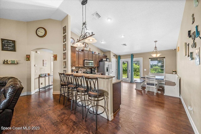 kitchen with dark wood-type flooring, a breakfast bar area, appliances with stainless steel finishes, lofted ceiling, and hanging light fixtures