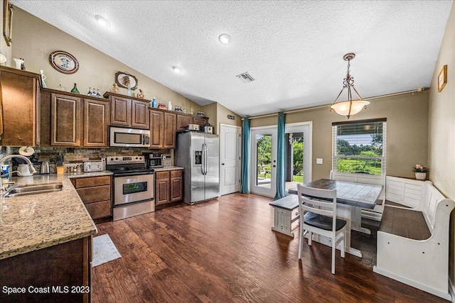 kitchen with appliances with stainless steel finishes, lofted ceiling, backsplash, hanging light fixtures, and dark hardwood / wood-style floors