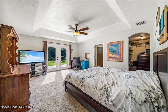 bedroom with french doors, ceiling fan, access to outside, a tray ceiling, and light carpet